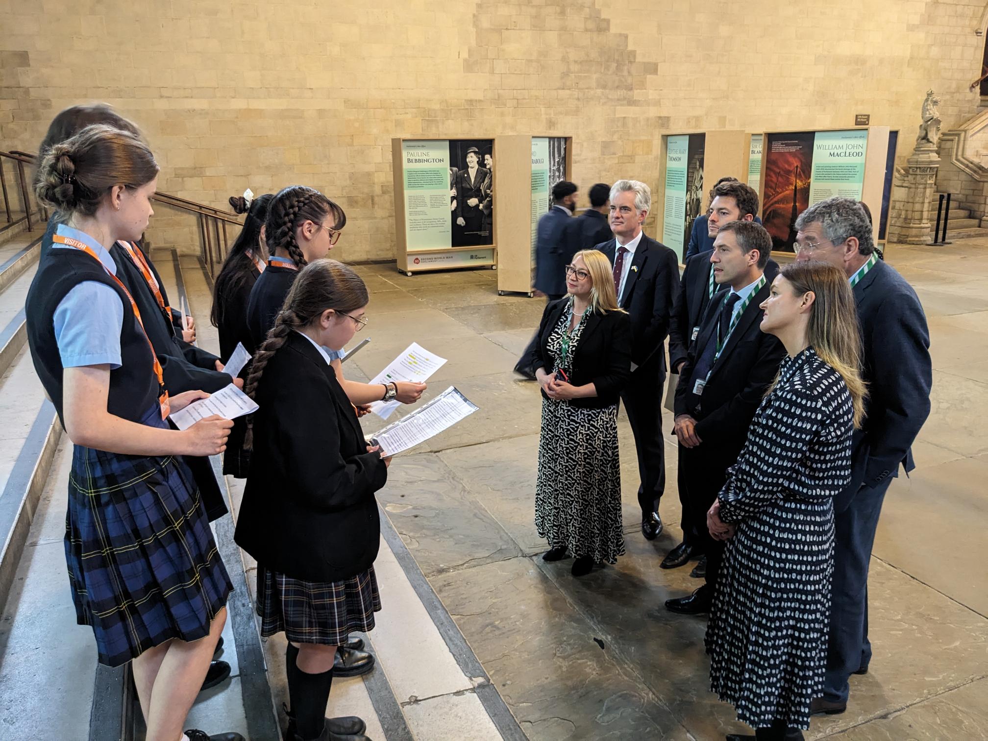 A group of school pupils reading from sheets of paper in front of a group of MPs in a large hall in Westminster.