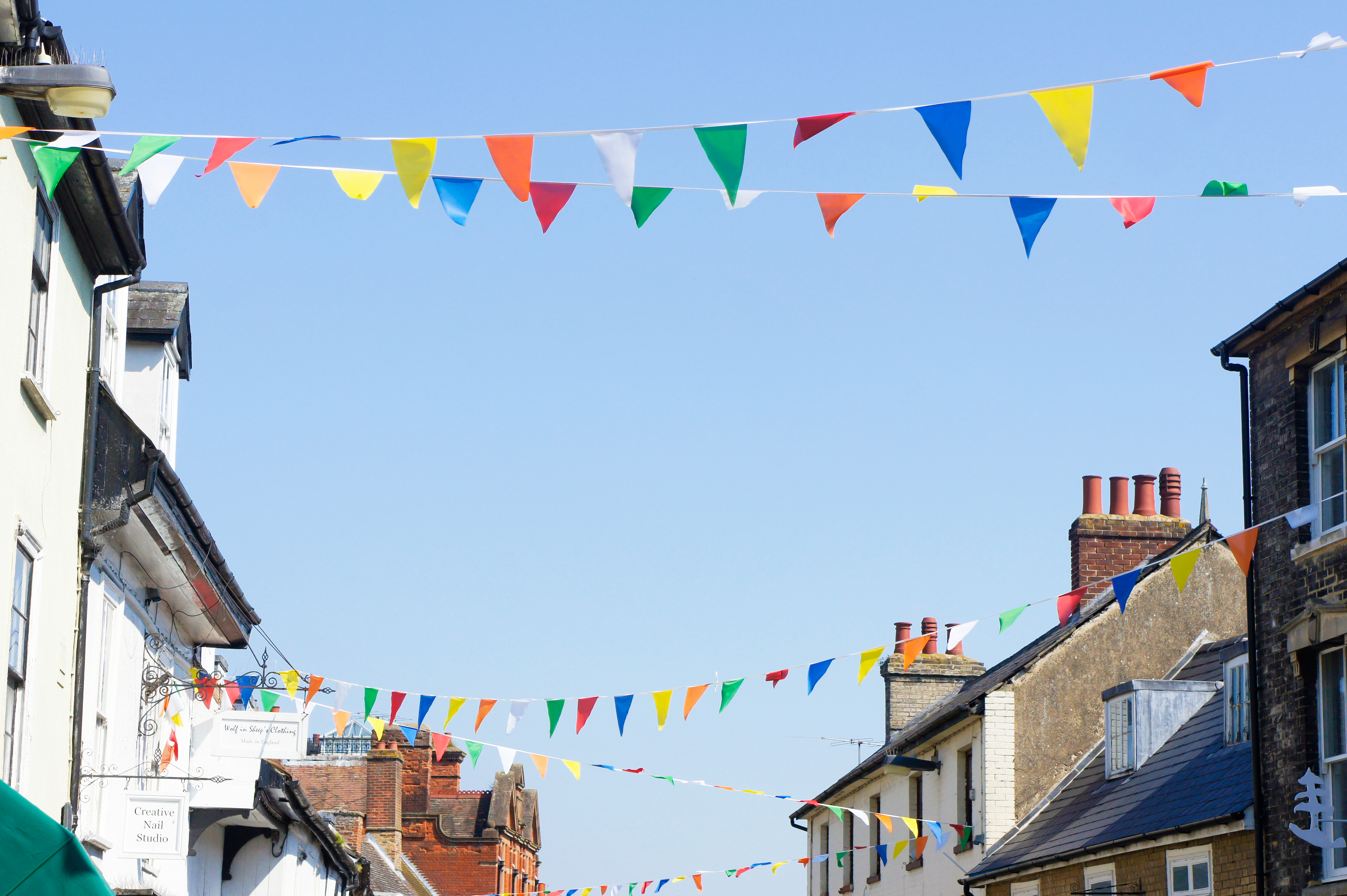 Colourful bunting between buildings in Bury St Edmunds with blue sky behind. 