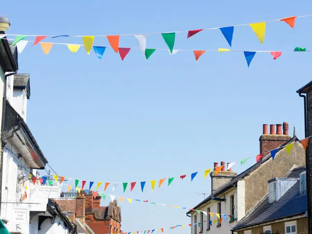 Colourful bunting between buildings in Bury St Edmunds with blue sky behind.