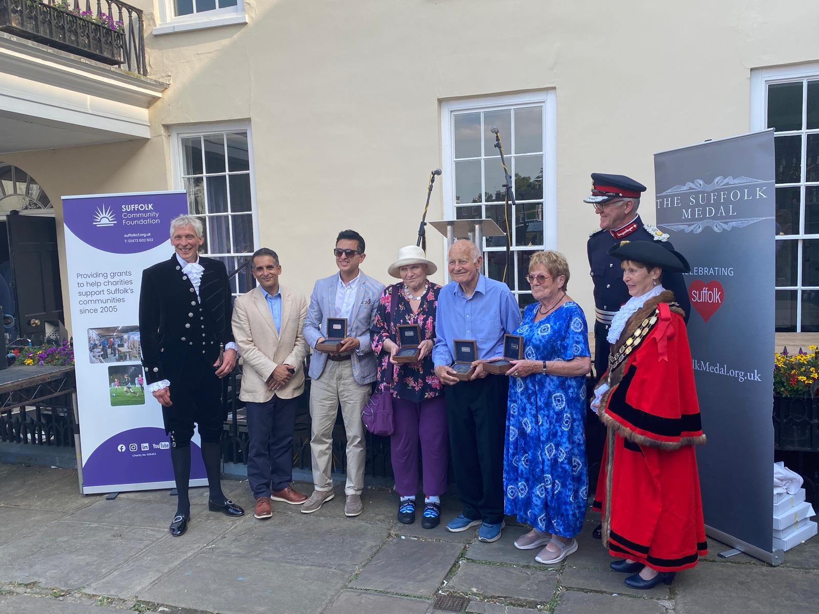 A line of people dressed smartly some holding boxes with Suffolk Medals they have been presented with